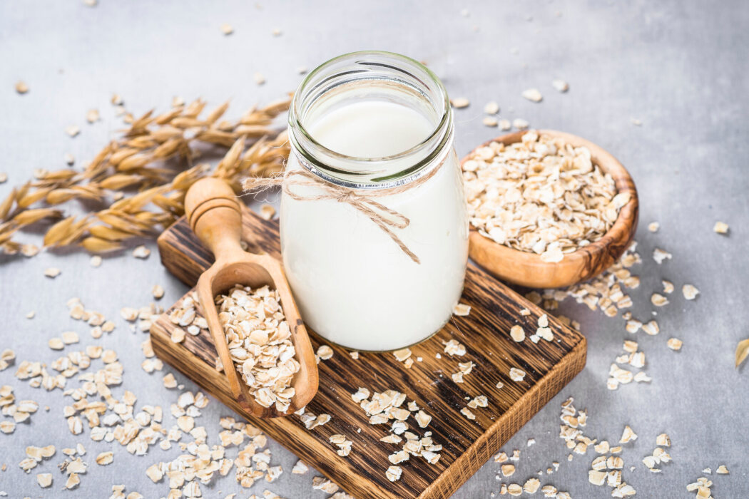 A glass of oat milk with oats and oat stalks.