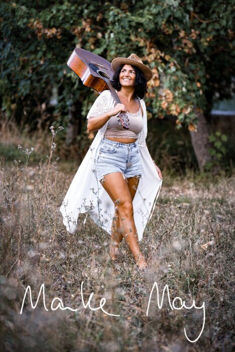 Singer-songwriter Maike May with a guitar outdoors.