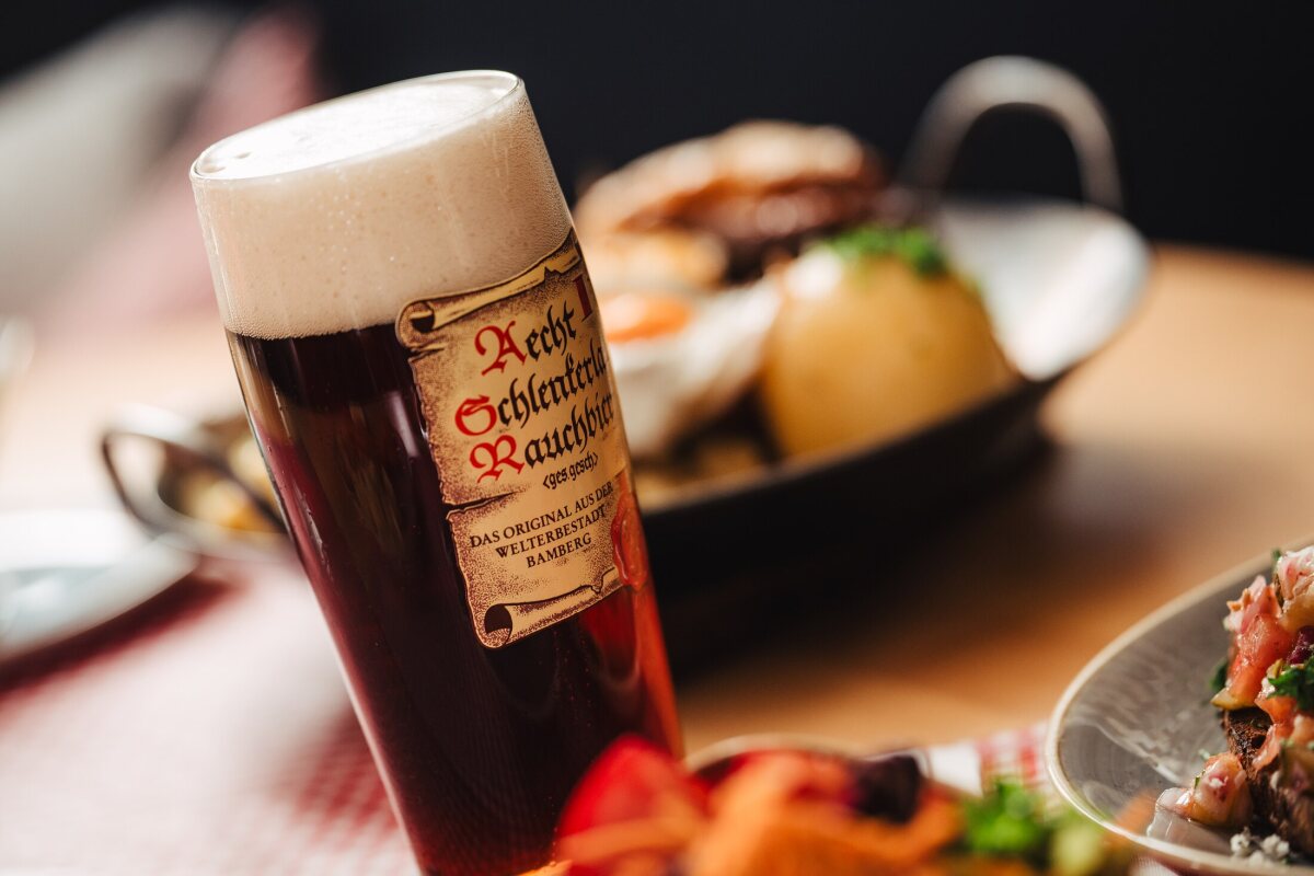 A glass of Bamberg smoked beer with a foamy head beside Franconian dishes at Café Zeis.