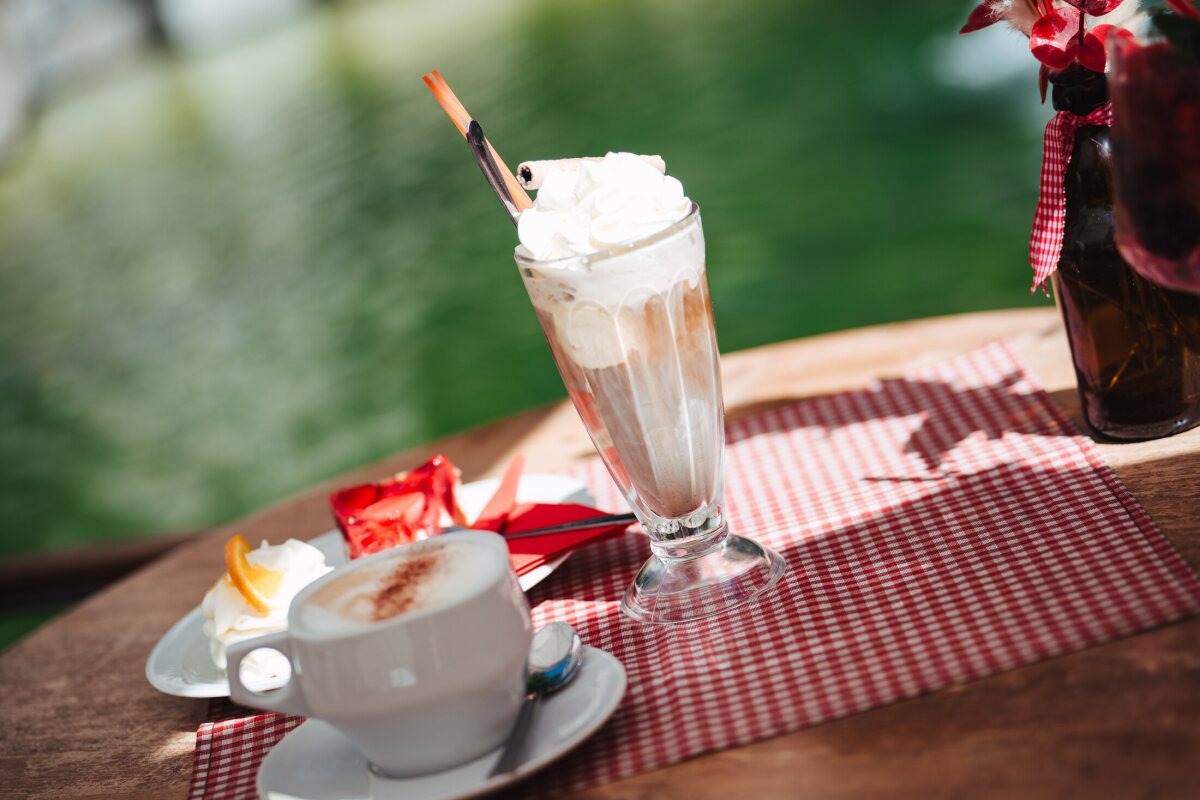Iced coffee with whipped cream and a cup of coffee on a terrace table by the fountain.