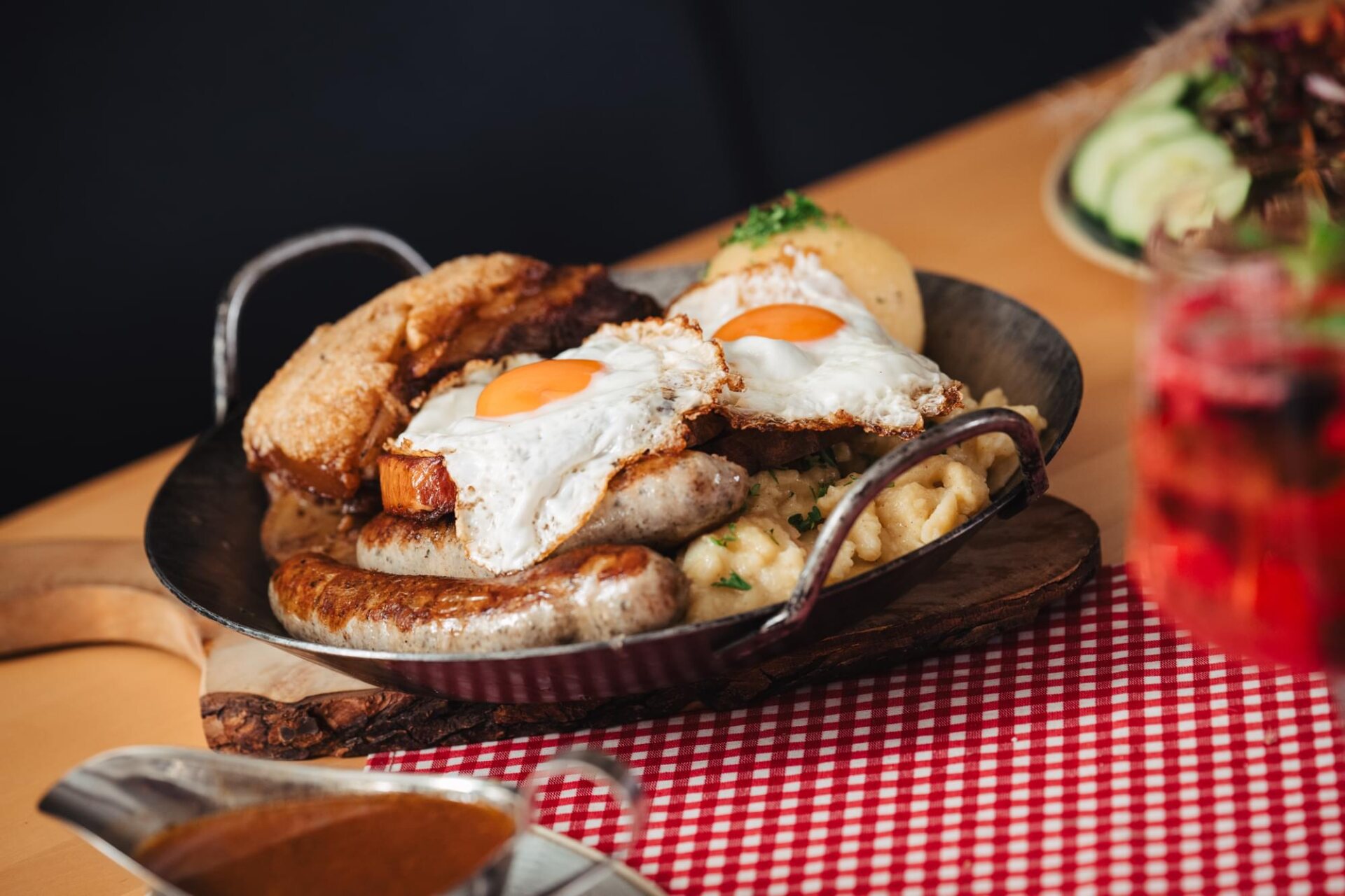 Fränkische Hausmannskost mit Bratwürsten, Spiegeleiern, Spätzle und Kloß, serviert in einer Pfanne auf der karierten Tischdecke.