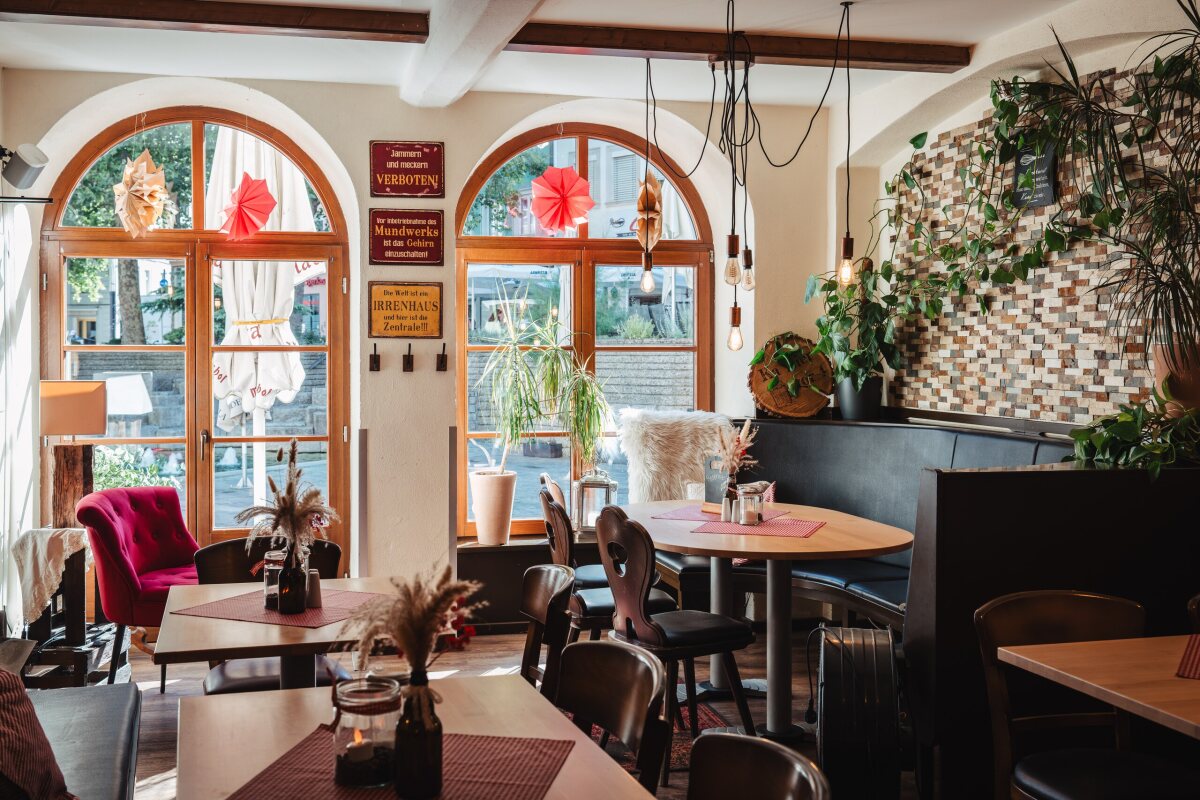 Heller Gastraum des Restaurant Café Zeis mit Rundbogenfenstern, Pflanzen und gemütlichen Sitzplätzen.