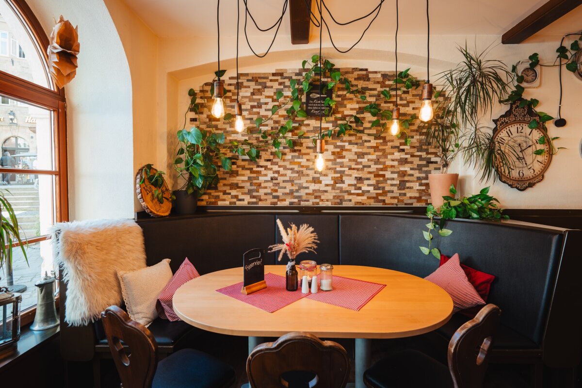 Gemütliche Sitzecke mit rundem Holztisch, Kissen und Pflanzen am Fenster des Café Zeis.